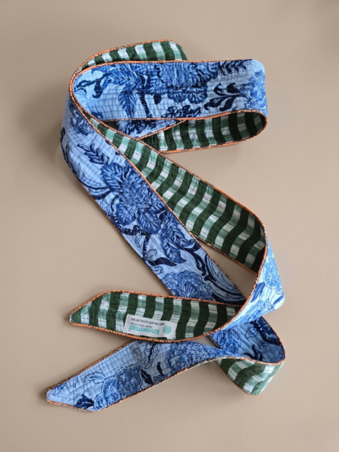 A handmade quilted cotton belt with a reversible design, showing a blue floral print on one side and green checks on the other, as seen in Gemini_Generated_Image_(229).jpg.