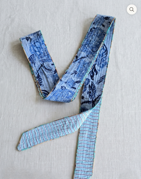 A handmade quilted cotton belt with a reversible design, showing a blue floral print on one side and a light blue striped pattern on the other, as seen in Gemini_Generated_Image_(232).jpg.
