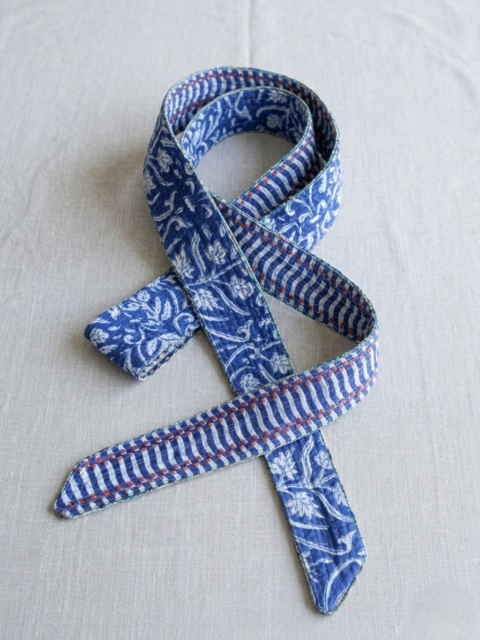 A handmade quilted cotton belt with a reversible design, showing a blue floral vine print on one side and a blue and white chevron stripe pattern on the other, as seen in Gemini_Generated_Image_(234).jpg.