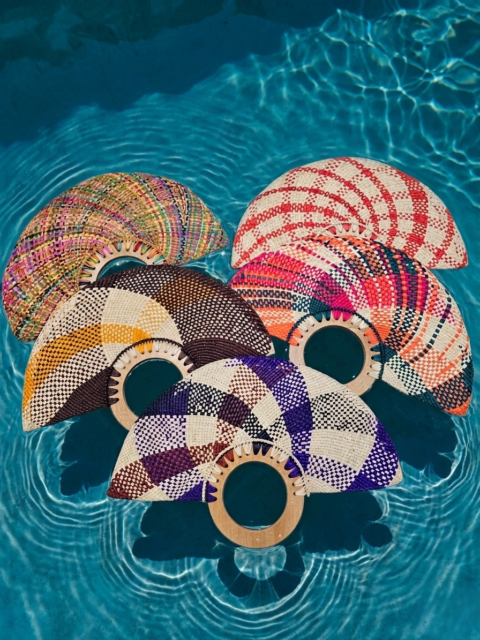 Vibrant handmade Colombian Iraca palm fans with circular wooden handles displayed over blue water.