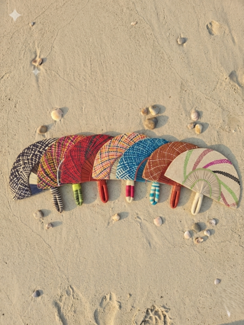 A row of colorful handwoven Colombian Iraca palm fans resting on white beach sand.